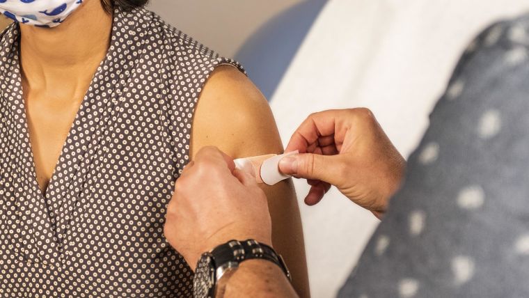 Inside a clinical setting, a plaster has been placed on the injection site of a patient who just received a vaccine.